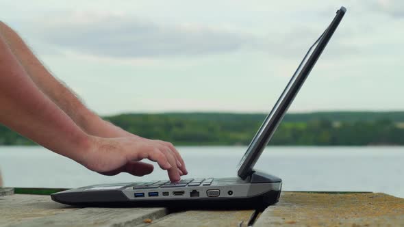 Man's hands using laptop computer. Young man using laptop on the pier.