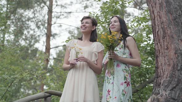 Two Beautiful Women with Wild Flowers Standing at Wooden Stairs, Talking, Smiling