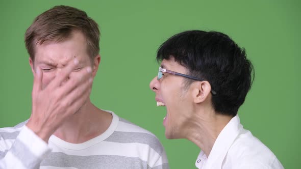 Young Angry Asian Businessman Screaming at Young Scandinavian Businessman While Covering Ears