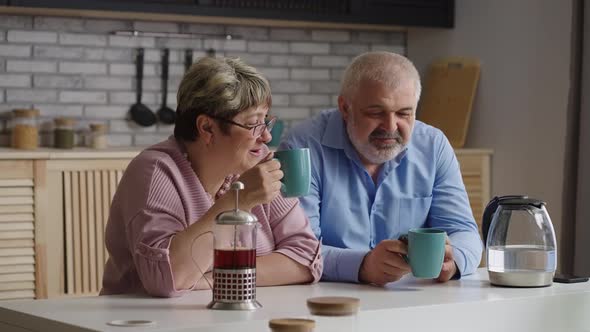 Cheerful Old Man and Woman are Drinking Tea at Weekend Relaxing at Home Kitchen Happy Retirees are