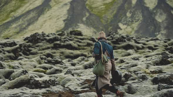 Man Walking Over Rocks In Greatcoat With Guitar Case