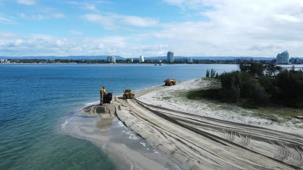 Unique drone view of heavy machinery working on a coastal sand replenishment project close to a urba