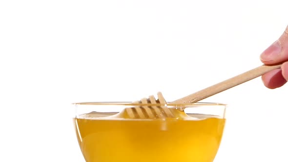 Hand Taking Honey From Bowl Using Wooden Spoon Dipper, Pit It Up, on White, Slow Motion