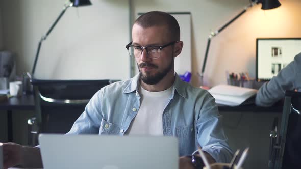 Young Caucasian Businessman Working with Computer and Drinking Coffee at Workplace in Office