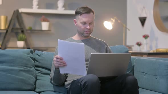 Casual Man with Laptop Working on Documents on Sofa