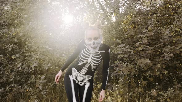 A girl with a scary make-up in a skeleton costume, a mask with rhinestones in a gloomy autumn forest