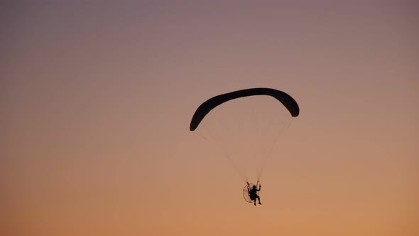 Dark Silhouette of Moto Paraglider Flies, Soars in the Air, Against the Background of a Bright