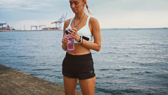 Young Disabled Woman Drinking Water From Sport Bottle on Pier After Training