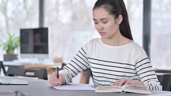 Young Asian Woman Doing Paperwork with Book in Office