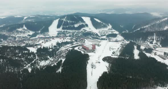 Aerial View of Ski Slopes with Skiers and Ski Lifts on Ski Resort in Winter Forest Against Snowy