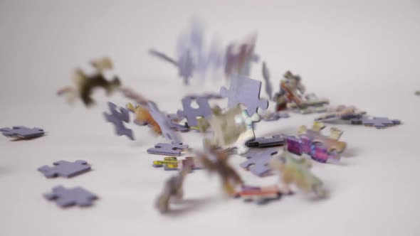 Close-ups of jigsaw puzzle pieces fall in slow motion onto a white background, filling the entire