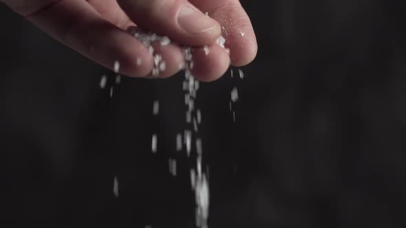 Hand adding white salt on a black background