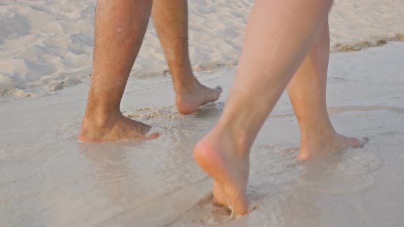 Man and Female Legs Wandering on the Water on the Beach.