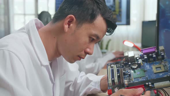 Asian Male Engineer Inspects Printed Circuit Board Motherboard. Scientist Designs Industrial Pcb