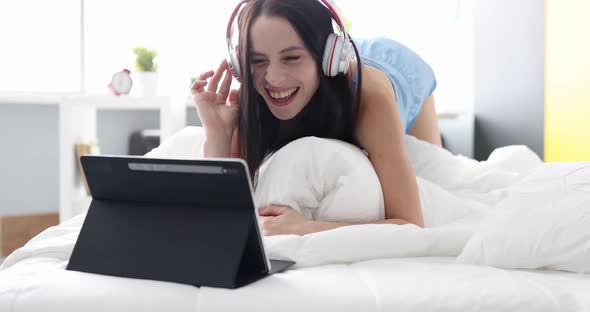 Happy Woman in Headphones Listening to Music From Tablet and Dancing at Home in Bed