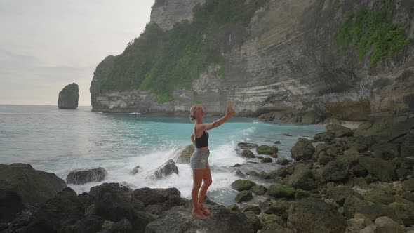 Happy blond travel girl taking selfie on Tembeling beach with tall cliffs