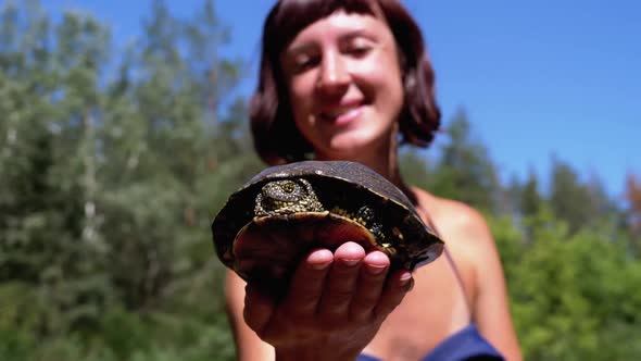 Woman Holds Funny Turtle in Arm and Smiles on River with Green Vegetation