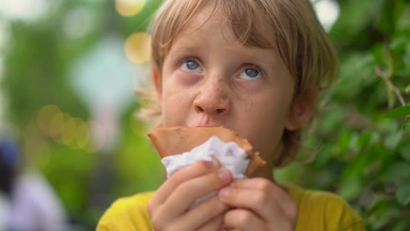 Closeup Shot of a Little Boy Eating a Tasty Pancake on a Street Market. Street Food Concept.