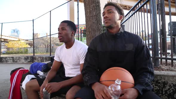 Two young basketball players drinking water while taking a break from playing.