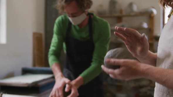 Male and female potter wearing face mask and apron kneading the clay at pottery studio