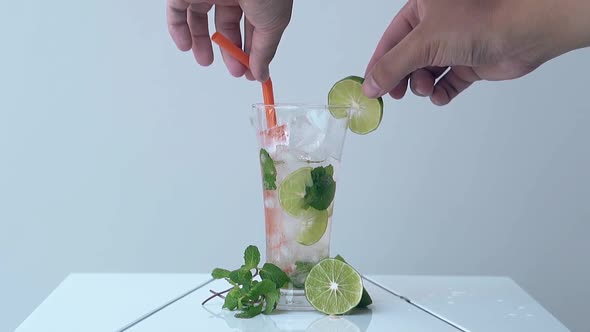 Man Takes Out Straw and Lime Slice From Glass on White Table