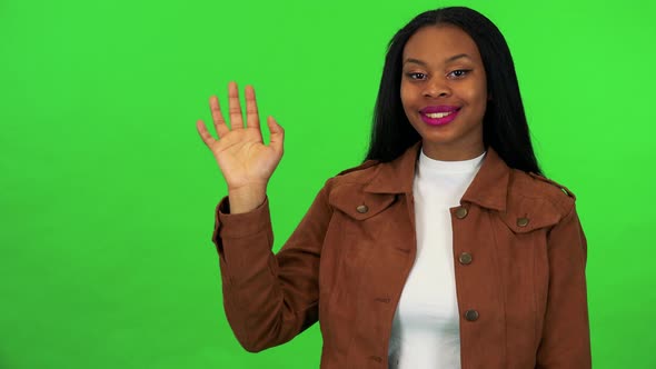 A Young Black Woman Smiles and Waves at the Camera - Green Screen Studio