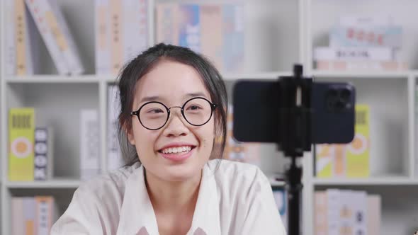 Happy young Asian woman wearing glasses, sitting and selling clothes by live broadcasting