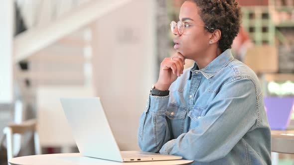 Pensive African Woman Thinking and Working on Laptop at Cafe