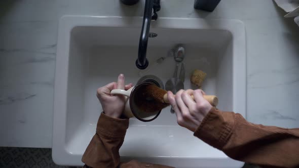 woman washes a cup in the kitchen using eco-friendly brush