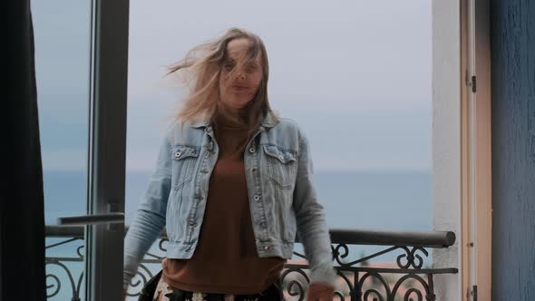 Young woman in a beige sweater stands on the balcony. Wind develops female’s hair, freedom concept