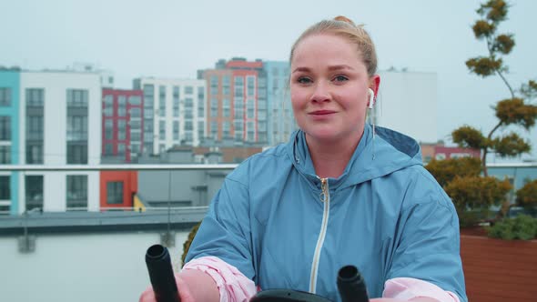 Healthy Caucasian Woman Exercising Workout on Stationary Cycling Machine Bike on House Rooftop Gym