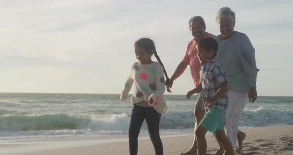 Happy hispanic grandparents and grandchildren walking on beach at sunset