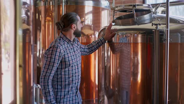 Portrait of Happy Male Brewer Admiring New Equipment in Brewery Smiling Walking at Large Beer Tanks