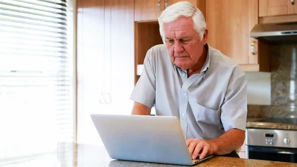 Senior man using laptop in the kitchen