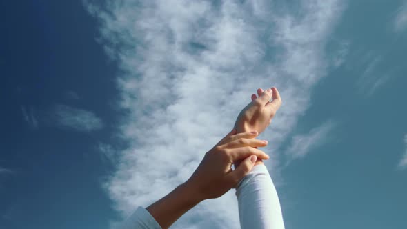 The Hands of a Young Girl are Frolicking Against the Background of a Blue Sky with Clouds