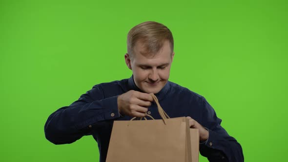 Man Taking Out Sale Discounts Inscription From Shopping Bags, Smiling Satisfied with Low Prices