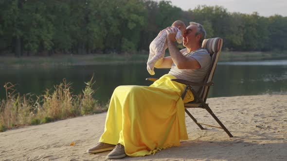 Grandfather Holding Newborn Baby Granddaughter Outdoors.