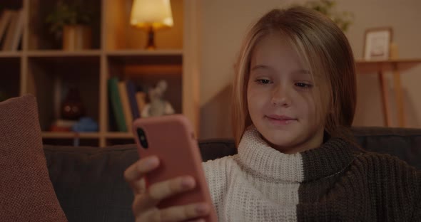 Crop View of Joyful Little Girl Touching Smartphone Screen While Sitting on Sofa at Home