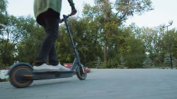 Woman and man ride electric scooter in public park, down back view. Couple is happy on romantic walk