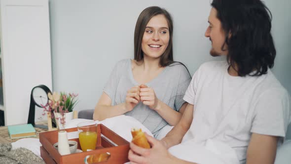 Man and Woman Chatting and Laughing During Romantic Breakfast in Bed at Home