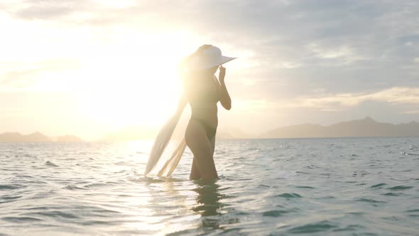 Woman In Bikini With Sun Hat Standing In Sea At Sunset