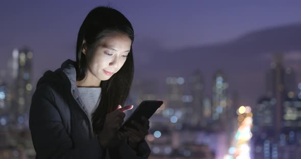 Woman using mobile phone over city background at night