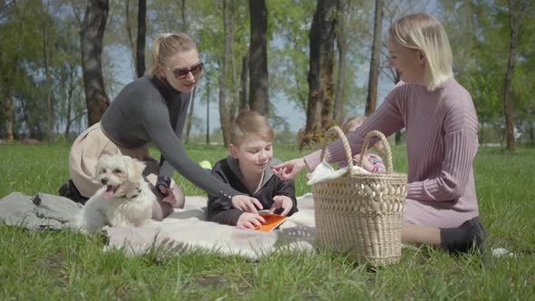 Portrait Two Young Cute Mothers with Them Kids Sit on the Blanket in Green Amazing Park on Nature on