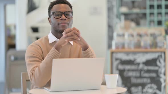 Creative African Man Smiling at Camera While Working on Laptop