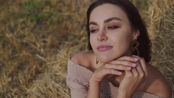 Portrait of Brunette Enjoys Posing While Relaxing on the Hay in a Windy Field