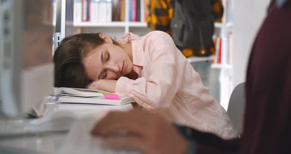 Young Tired Female Student Sleeping at Desktop in Library