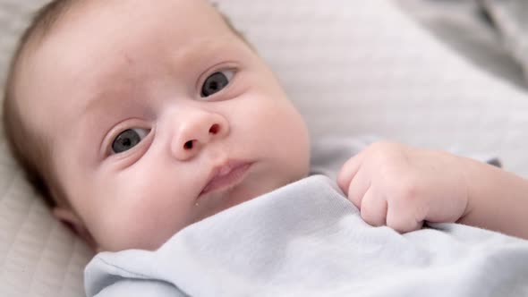 Dissatisfied Crying Upset Sad Newborn Baby Boy Lying in Nursery Cocoon with Blue Clothes on Bed in