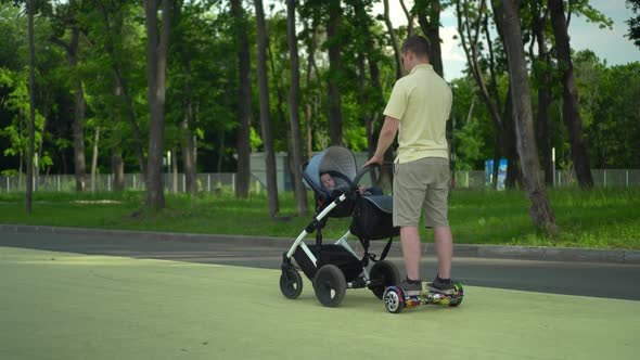 A Young Dad Walks with a Stroller on a Hoverboard in the Park