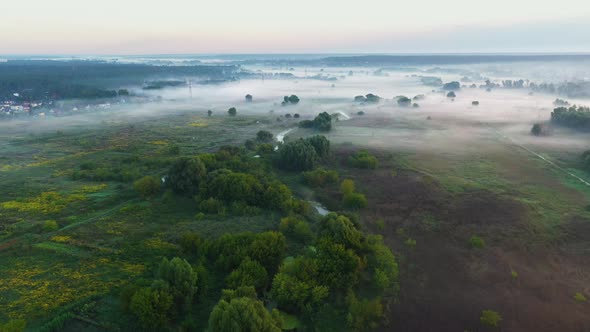 Bending river in a field on a foggy morning from aerial view.