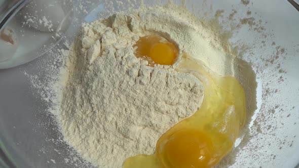 The yolk and white of the egg fall into the flour in a bowl. The dough preparation process.